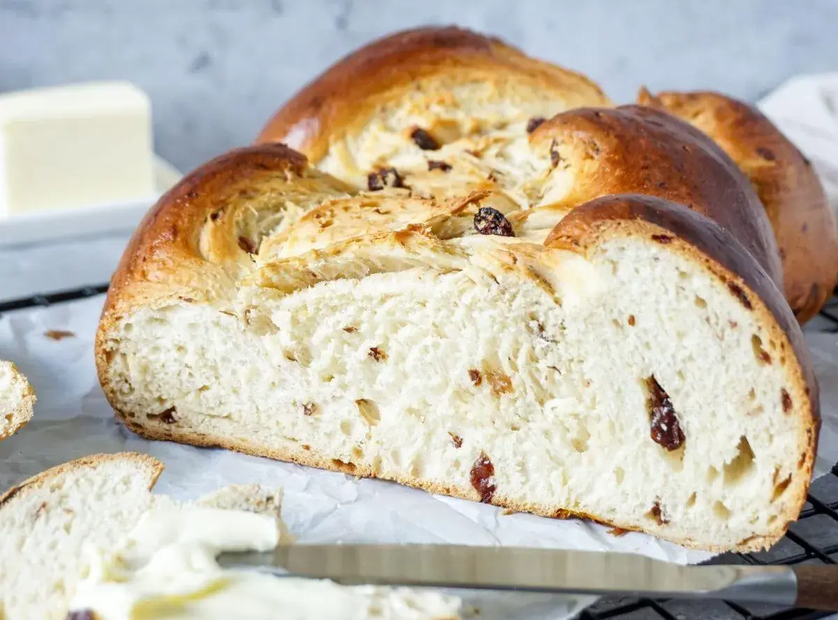 Ein goldbrauner Hefezopf mit Rosinen, frisch gebacken und bereit zum Genießen. Daneben liegt ein Stück Butter.