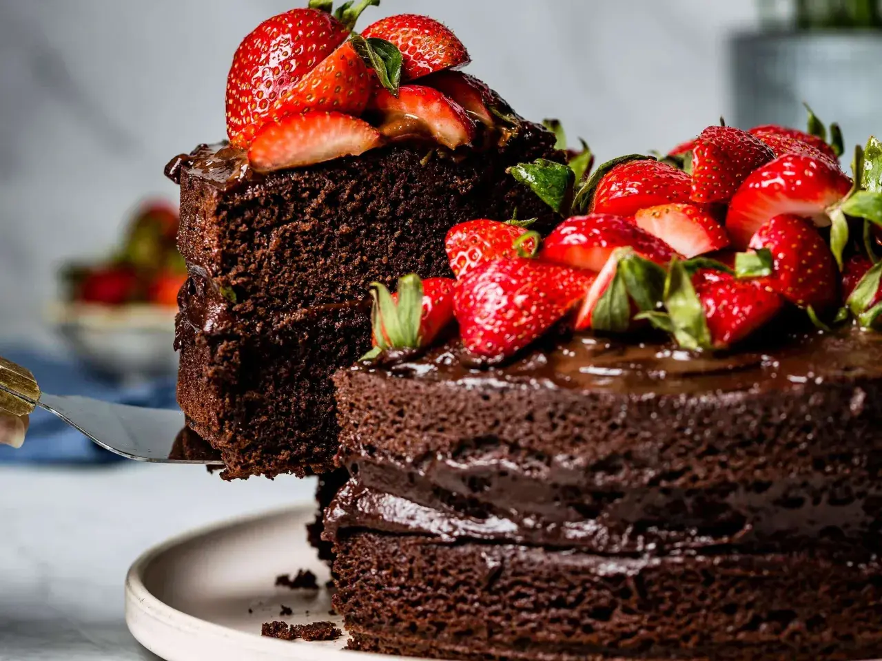 Ein hoher Schokokuchen mit frischen Erdbeeren und Schokoladenglasur wird angeschnitten.