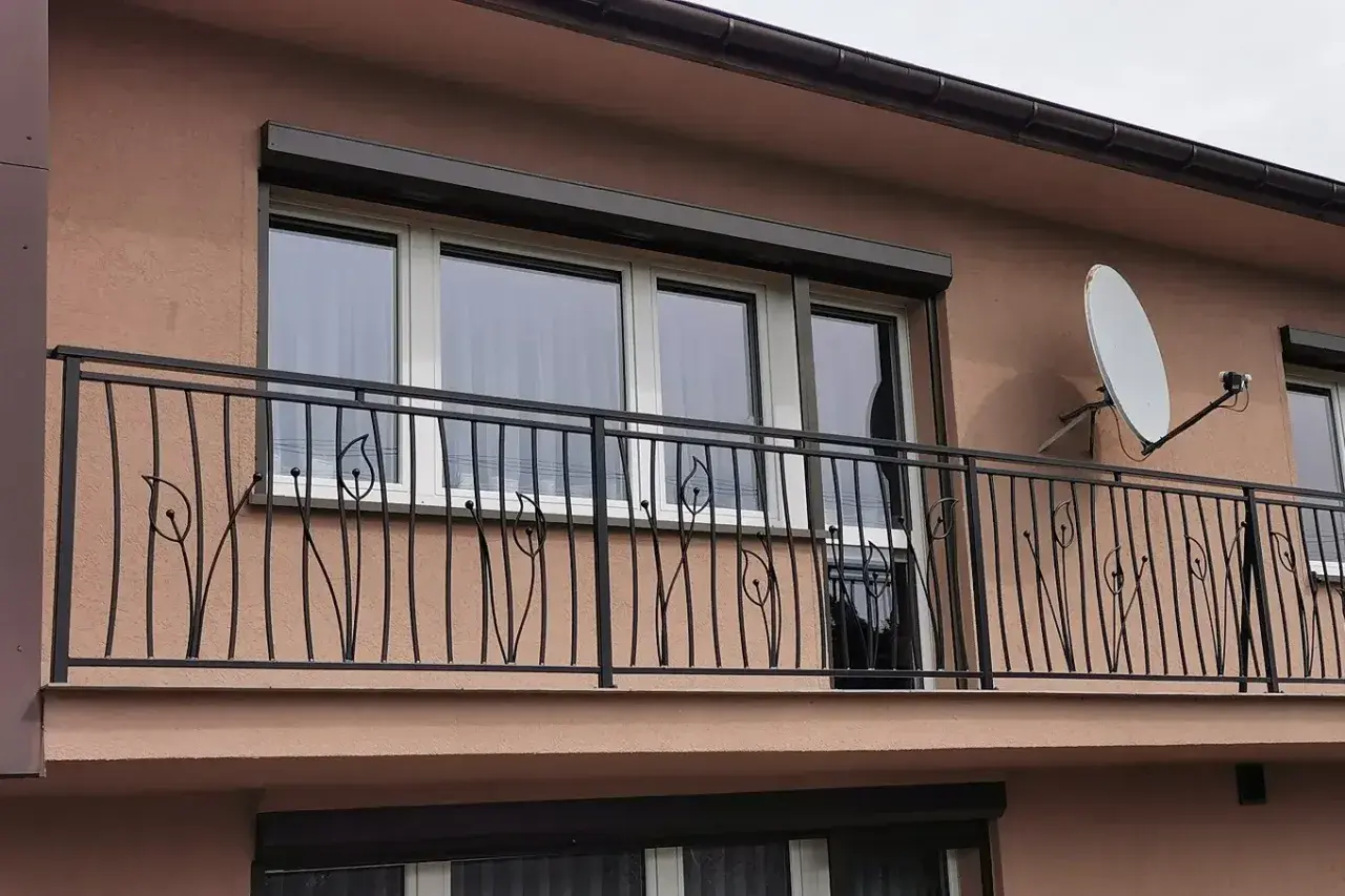 Elegancka, czyszczenie balustrady metalowej z motywem roślinnym. W tle okna i antena satelitarna.