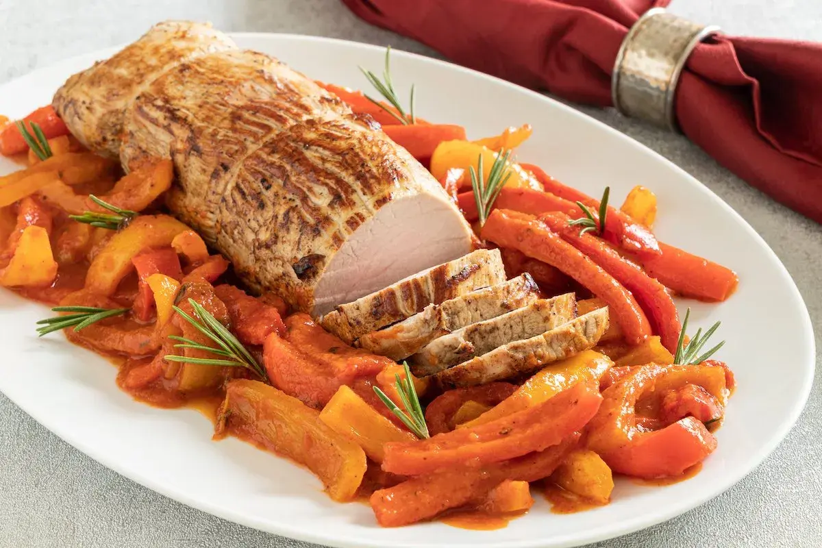 Arrosto di vitello in pentola con peperoni e carote, guarnito con rosmarino. Un piatto succulento e colorato.