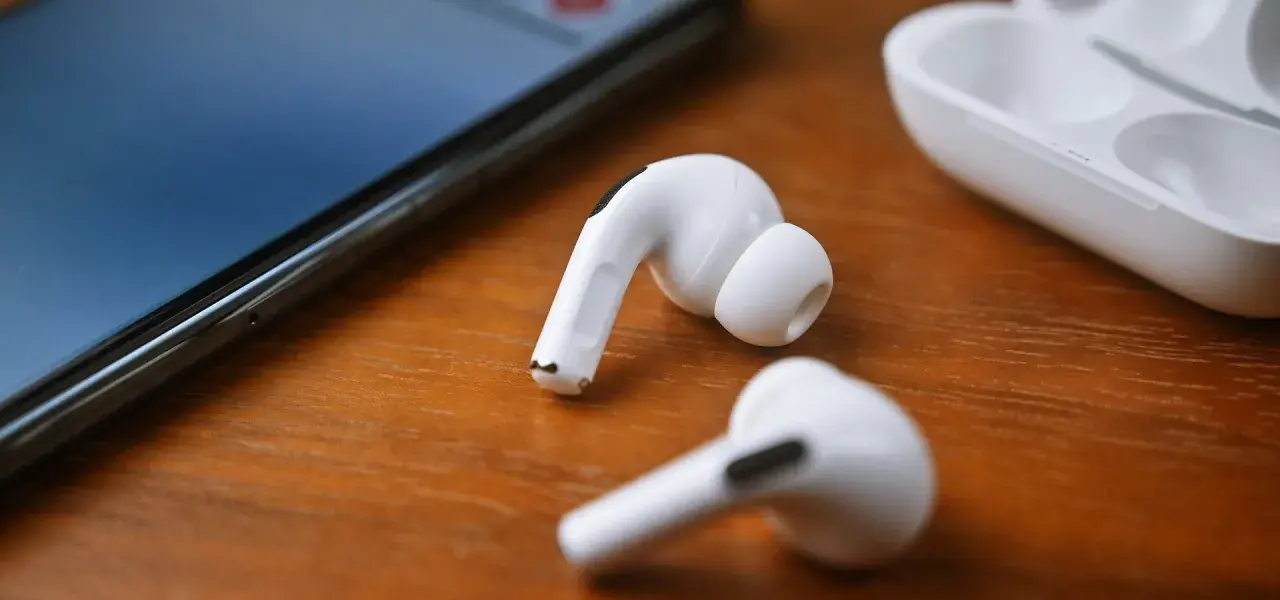 Białe słuchawki JBL leżą obok iPhone'a i etui. Dowiedz się, jak podłączyć słuchawki JBL do iPhone'a, by cieszyć się muzyką.