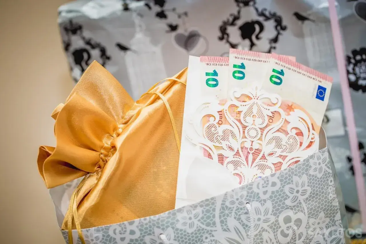 Złota sakiewka z prezentem i banknotami 10 euro, ozdobiona koronkową kartką. Idealny pomysł, jak zapakować zdrapki na wesele.