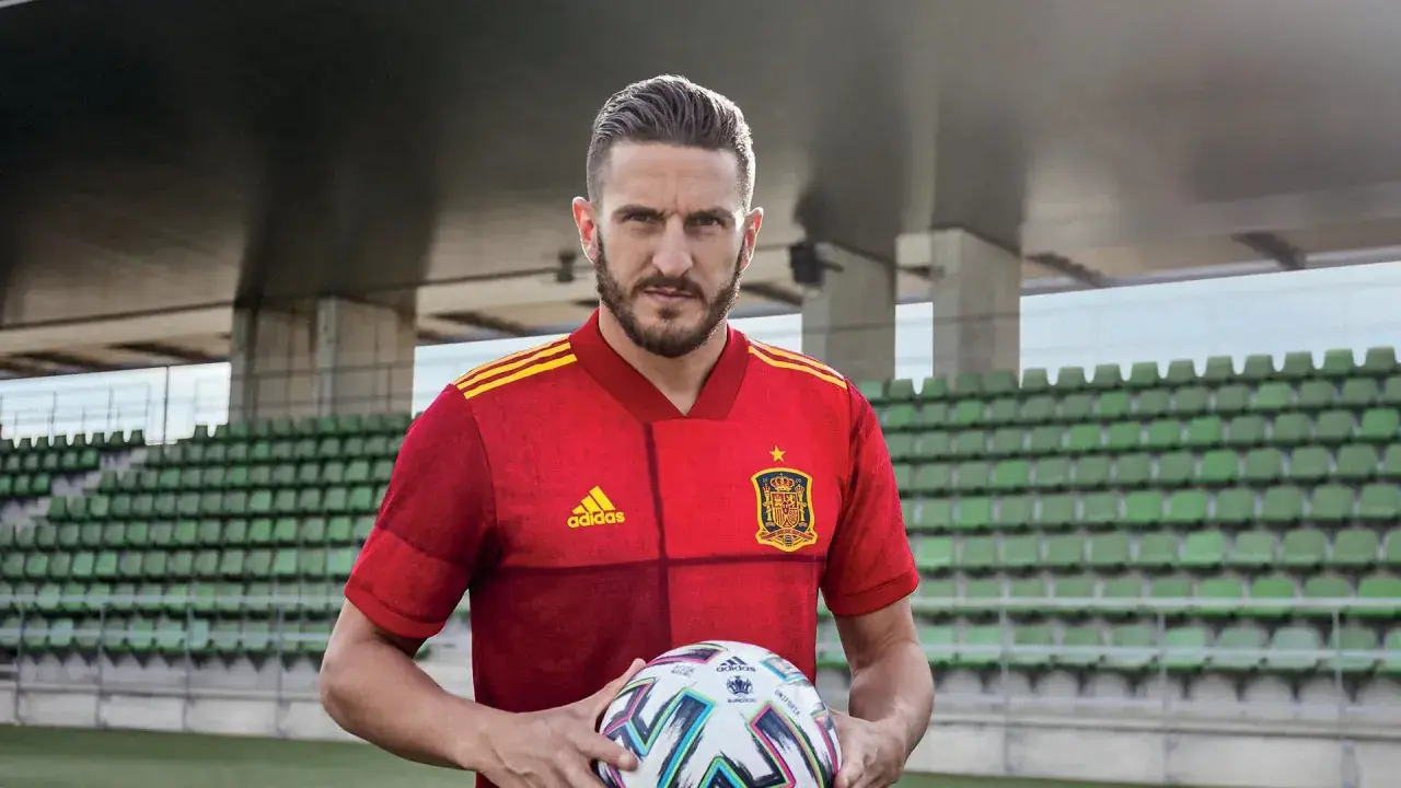 Piłkarz w czerwonej koszulce Hiszpanii z piłką, gotowy do gry w stylu tiki-taka.