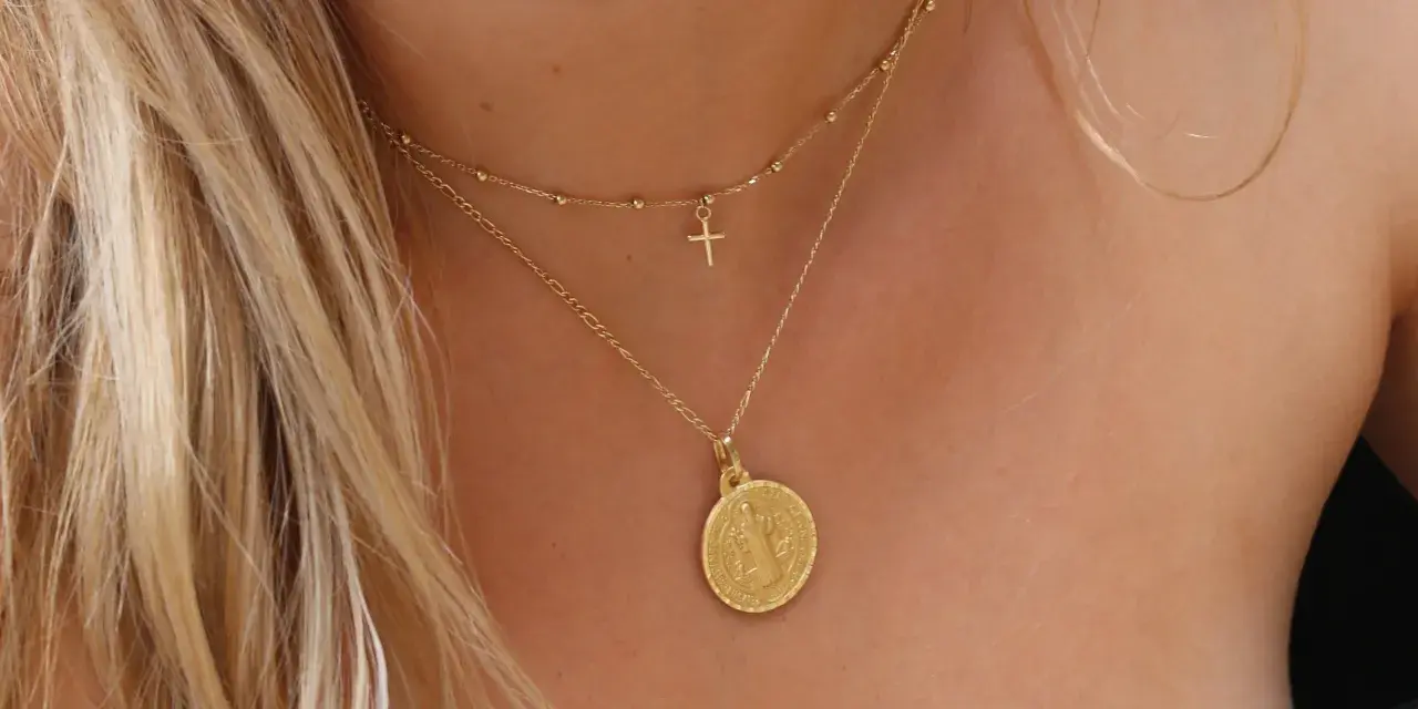 Elegante cadena de oro con medalla de San Benito y un pequeño crucifijo.