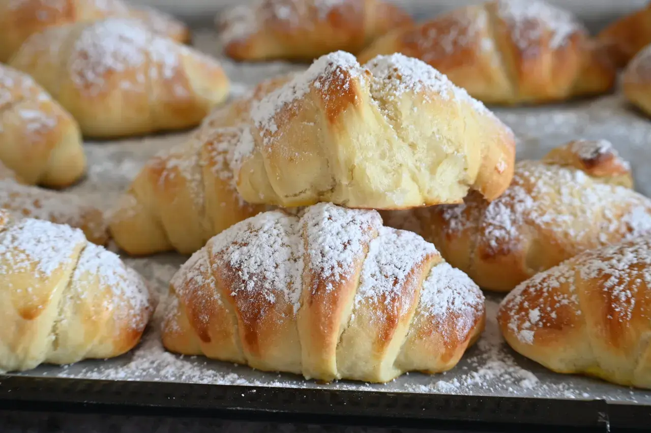 Brioches fatte in casa, dorate e soffici, cosparse di zucchero a velo. Un dolce profumo che invita a gustare la colazione.