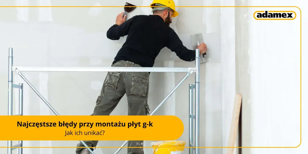 Budowlaniec w żółtym kasku i roboczych spodniach na rusztowaniu wygładza ścianę gładzią. Unikaj błędów przy montażu płyt g-k, jak przy nitowaniu.