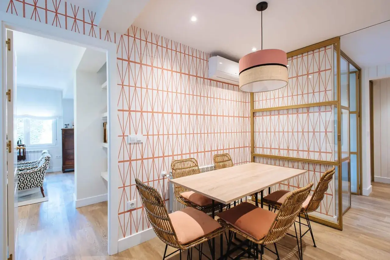 Comedor con papel pintado de rombos naranjas, mesa de madera y sillas de mimbre. Un ejemplo de como poner papel pintado para renovar tu hogar.