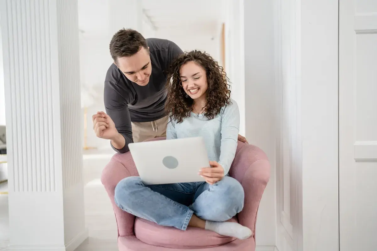 Para przygotowuje się do ślubu, korzystając z nauk przedmałżeńskich online. Uśmiechnięci patrzą na ekran laptopa.
