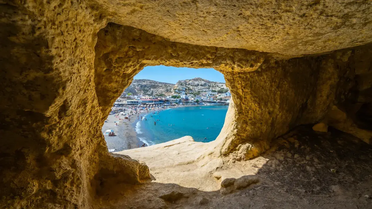 Blick durch eine Höhle auf einen belebten Strand und das türkisfarbene Meer. Ein perfekter Ausschnitt der Kreta Highlights.