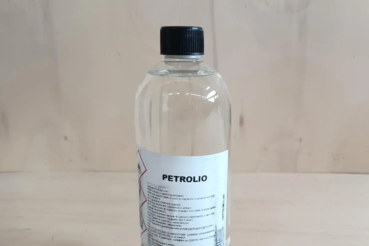 Bottiglia di **petrolio bianco su legno**. Liquido infiammabile, da usare con cautela.