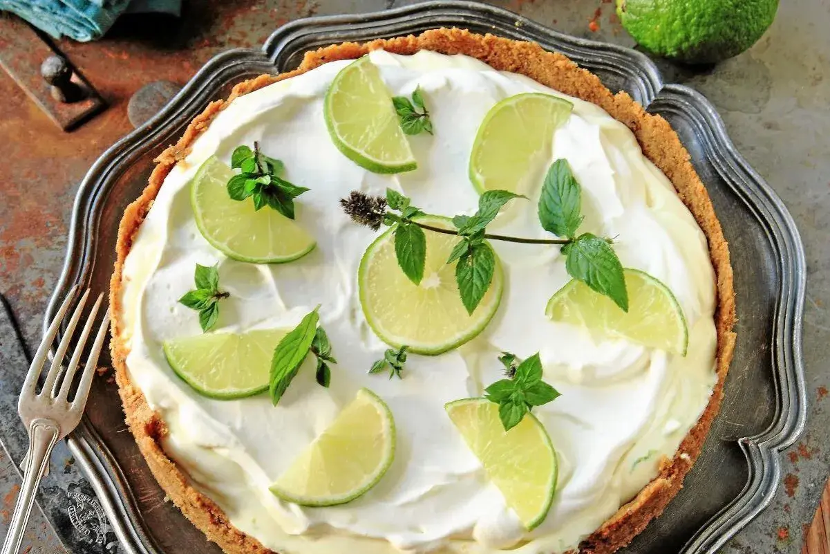 En krämig key lime pie med limeklyftor och mynta på en krispig botten.