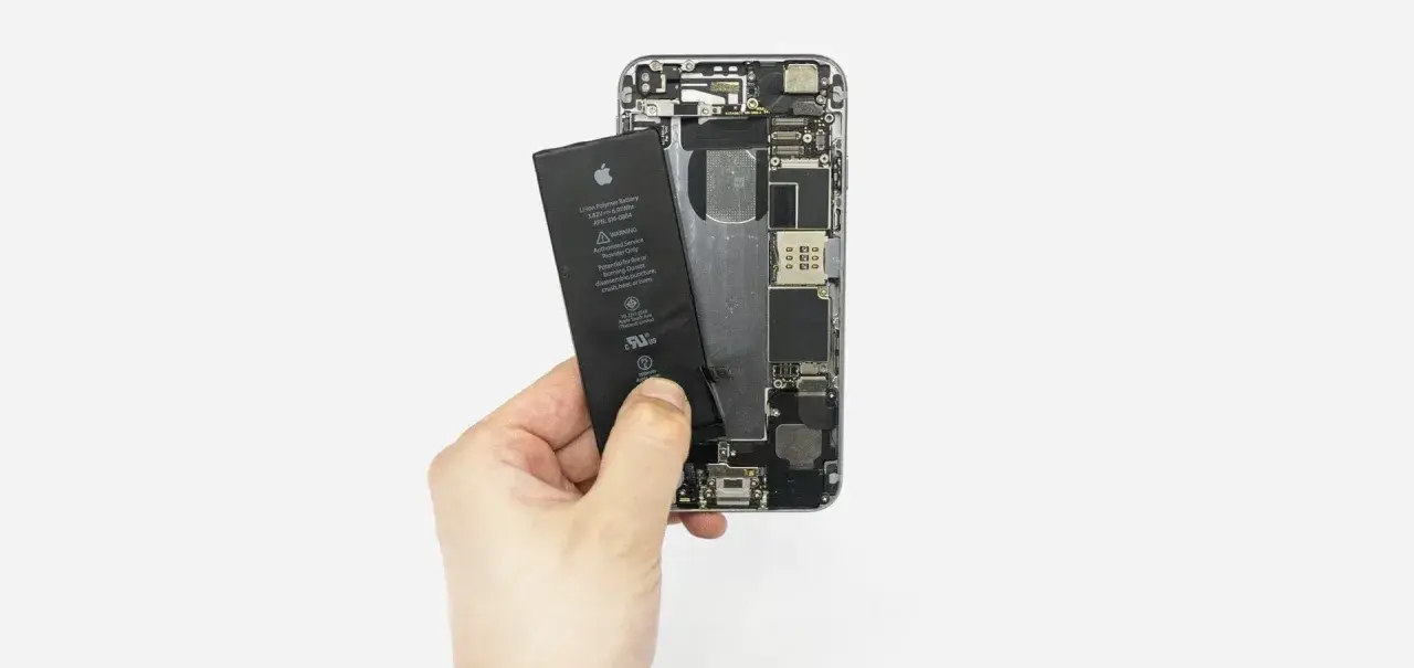 Dłoń wyjmuje baterię z otwartego iPhone'a 6s.