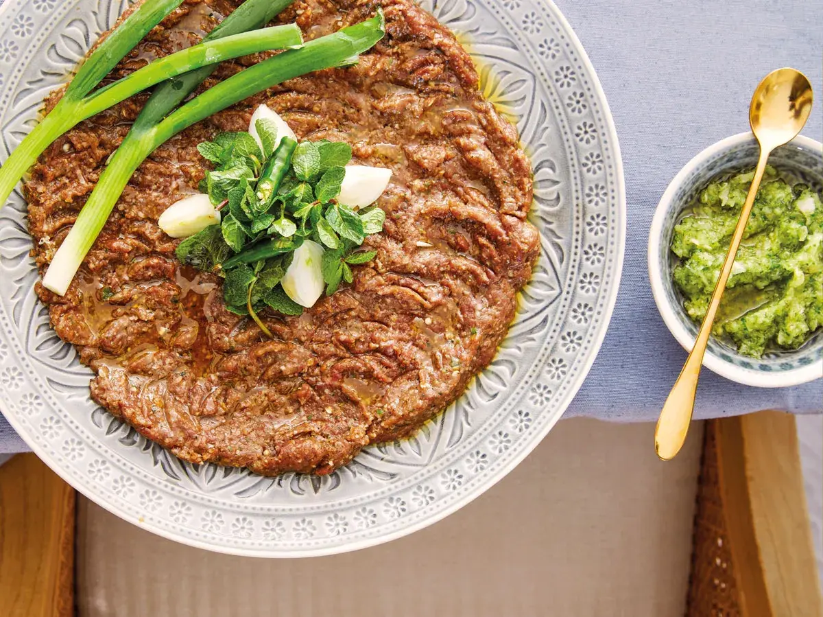 En tallrik med kibbeh nayyeh, rå köttfärs kryddad med bulgur och örter, toppad med vitlök, mynta och chili. Serveras med en grön sås.