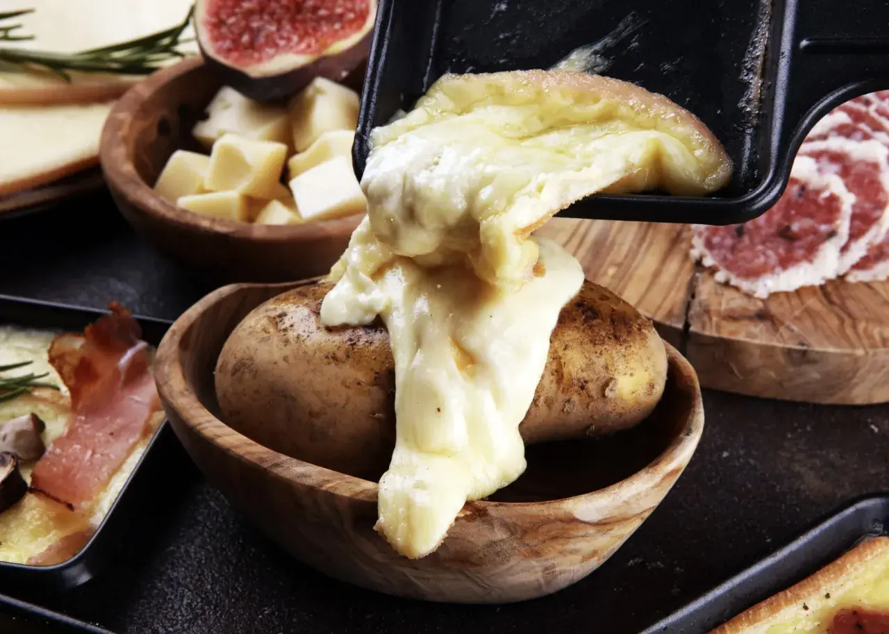 Fromage fondu coulant sur une pomme de terre, signe d'une raclette réussie. Accompagné de charcuterie et de figues.