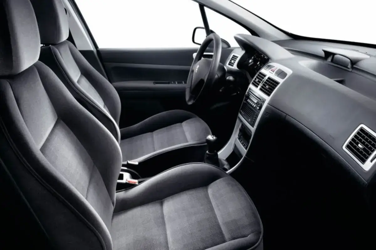 Interior de Peugeot 307, asientos delanteros de tela gris, salpicadero y consola central. Sin anomalia anticontaminacion visible.
