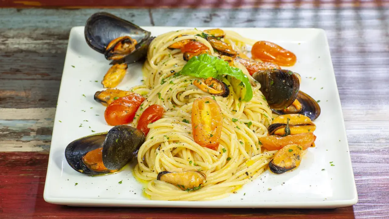 Un invitante piatto di spaghetti con le cozze e pomodorini, guarnito con basilico fresco.