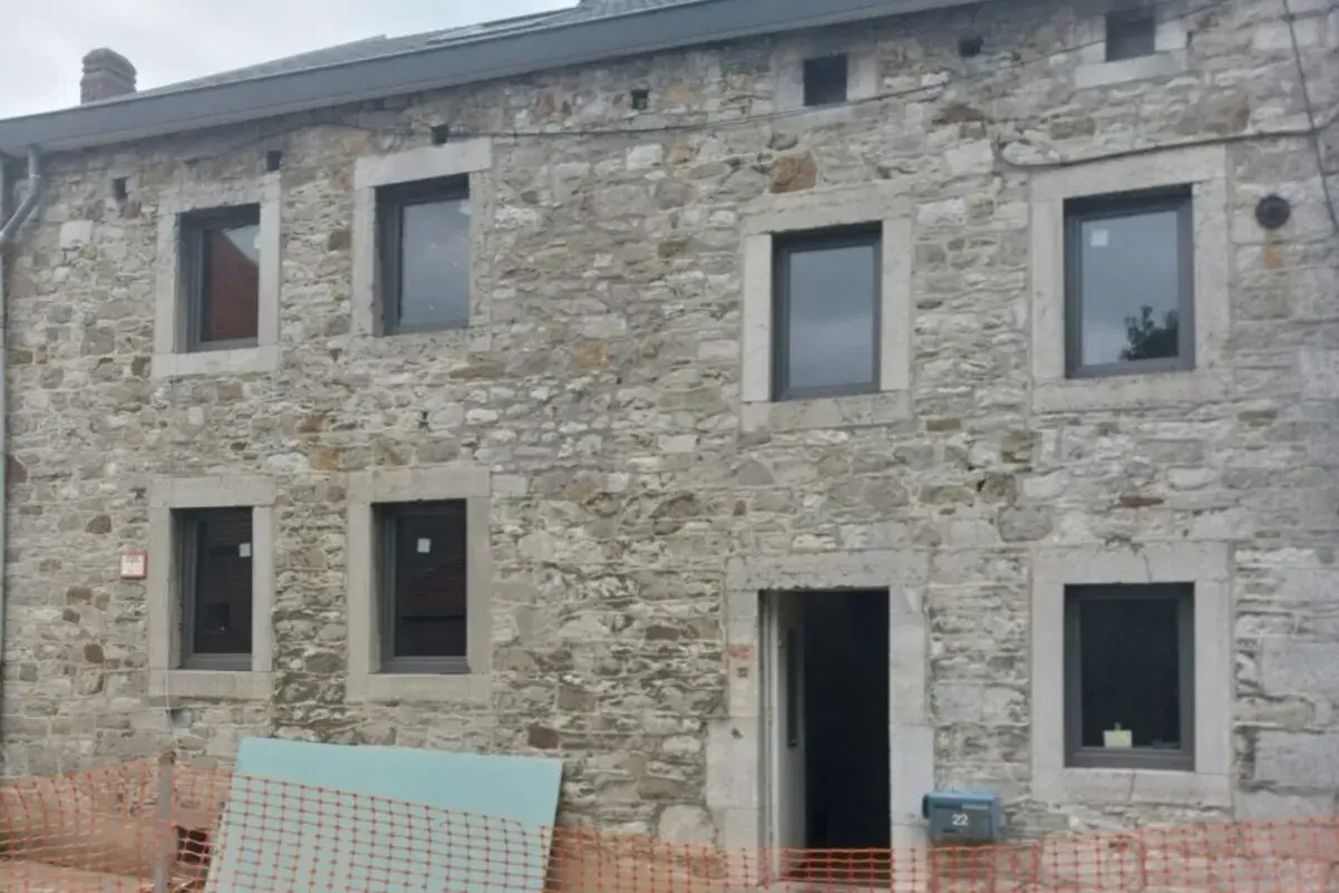 Façade d'une maison en pierre, en cours d'isolation. Fenêtres neuves et entrée ouverte sur un chantier.