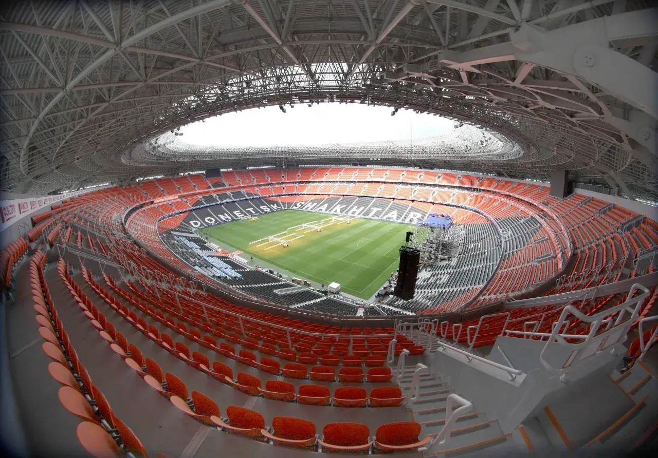 Pusta, nowoczesna arena stadionu Szachtara Donieck z pomarańczowymi i czarnymi siedzeniami oraz zieloną murawą.