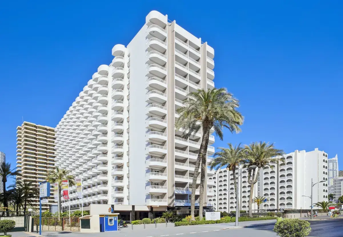 Edificio Sol con balcones curvos y palmeras bajo un cielo azul.