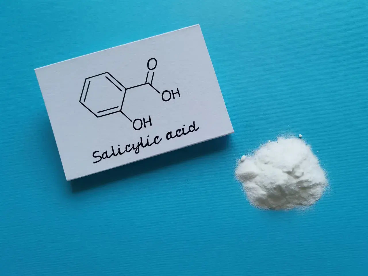 Kwas salicylowy na twarz: biały proszek i jego wzór chemiczny na kartce.