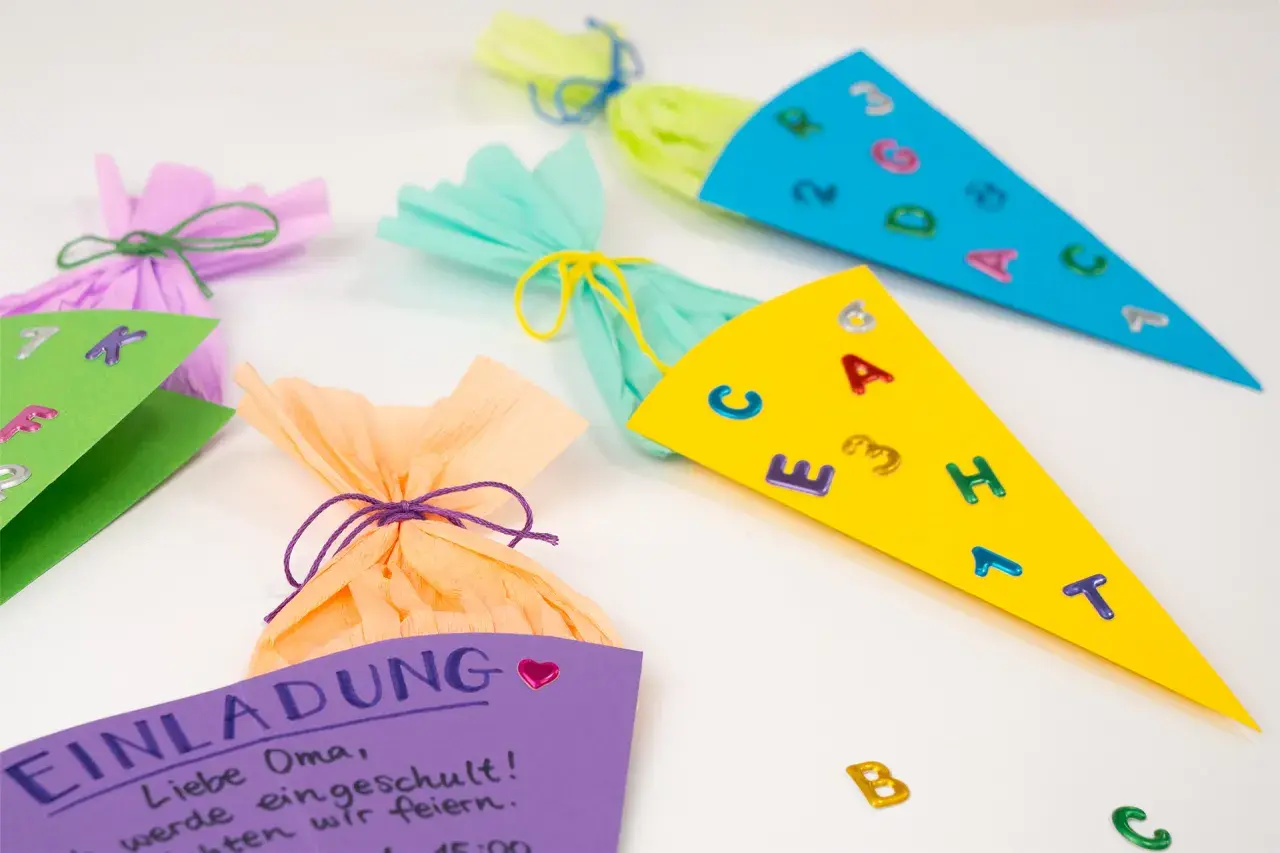Bunte Schultüten und eine Einladung zum Einschulungsfest basteln. Kleine Buchstaben und Zahlen zieren die Tüten.