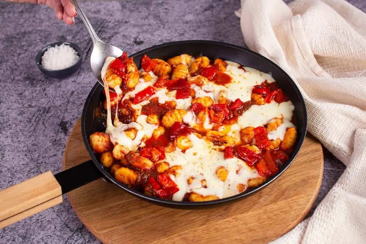 Gnocchis tomate mozza fondants, servis dans une poêle, avec une cuillère qui en prélève une portion filante.