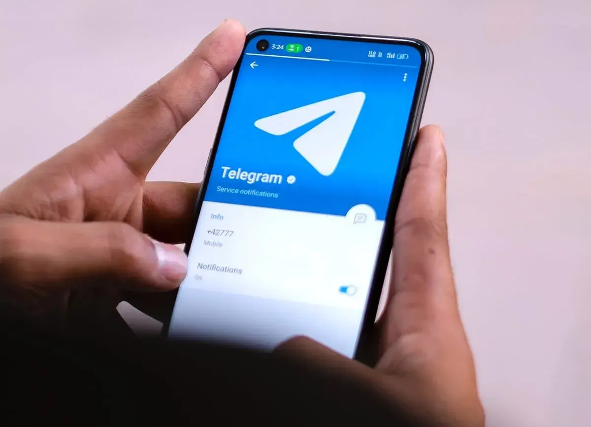 Dłonie trzymają smartfon z otwartą aplikacją Telegram. Widać logo i opcje powiadomień, idealne do dyskretnych rozmów w tajnych grupach Telegram.