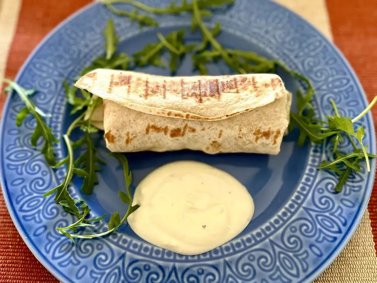 Ciepła tortilla z kurczakiem, podana z sosem i rukolą na niebieskim talerzu. Pyszne danie na szybki obiad.