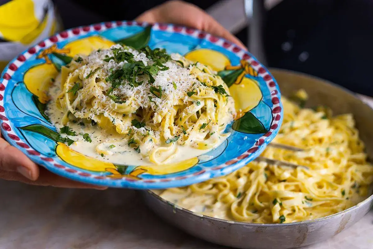 En tallrik med krämig pasta al limone, toppad med parmesan och persilja, serveras från en panna.