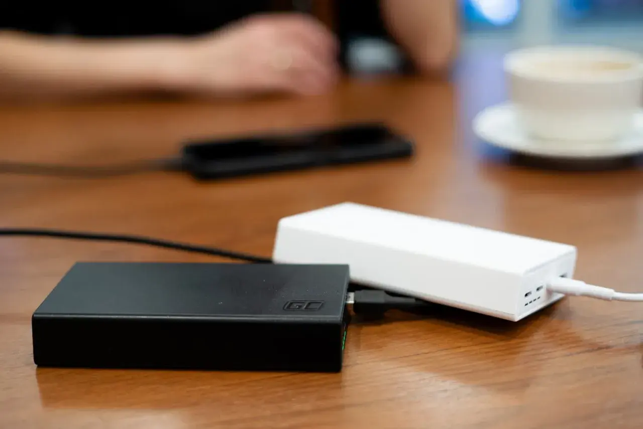 Dwa powerbanki, czarny i biały, leżą na drewnianym stole. W tle widać dłonie i filiżankę kawy. To idealny moment na sprawdzenie powerbank ranking.