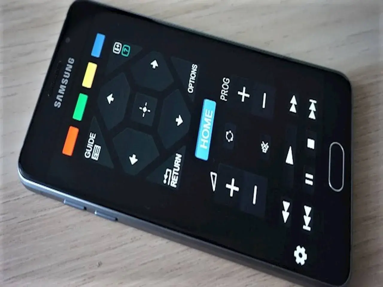 Smartfon z ekranem imitującym aplikację pilot do telewizora. Widoczne przyciski nawigacyjne, "HOME", "GUIDE", "RETURN" i inne funkcje.