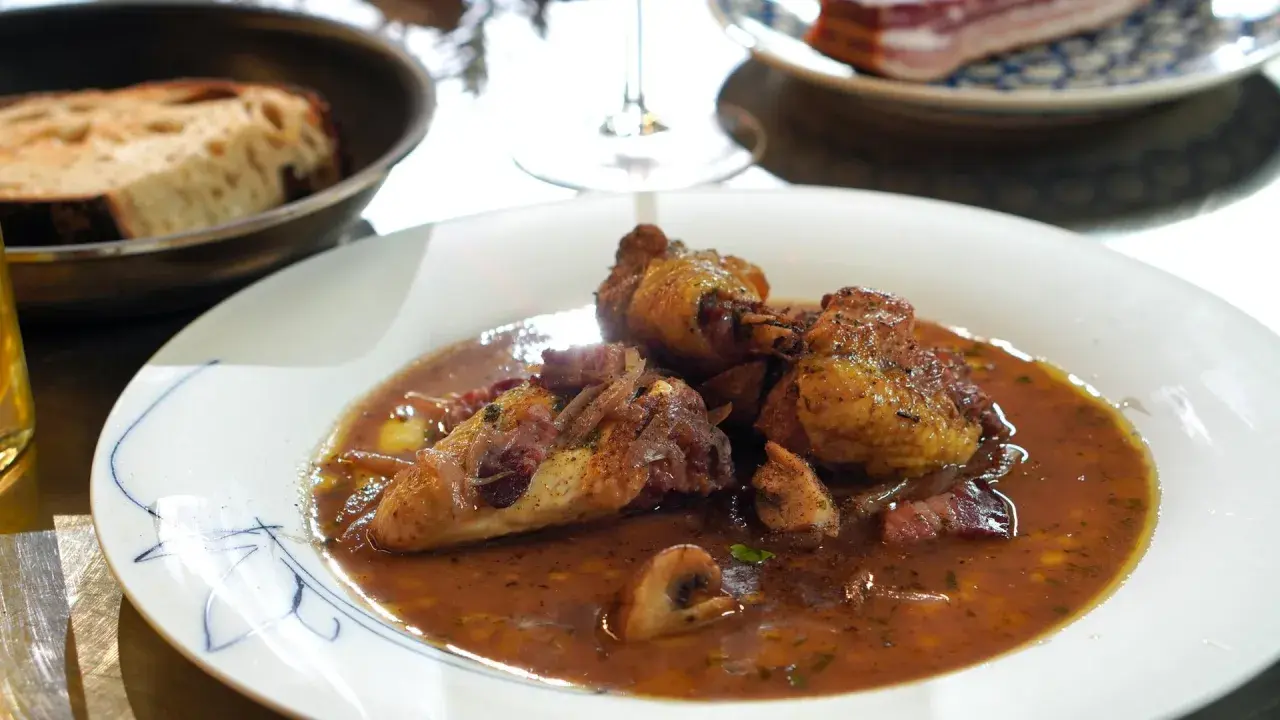 Ein köstliches Coq au Vin Rezept: zartes Hähnchen in Rotwein-Sauce mit Speck und Pilzen, serviert mit Brot.