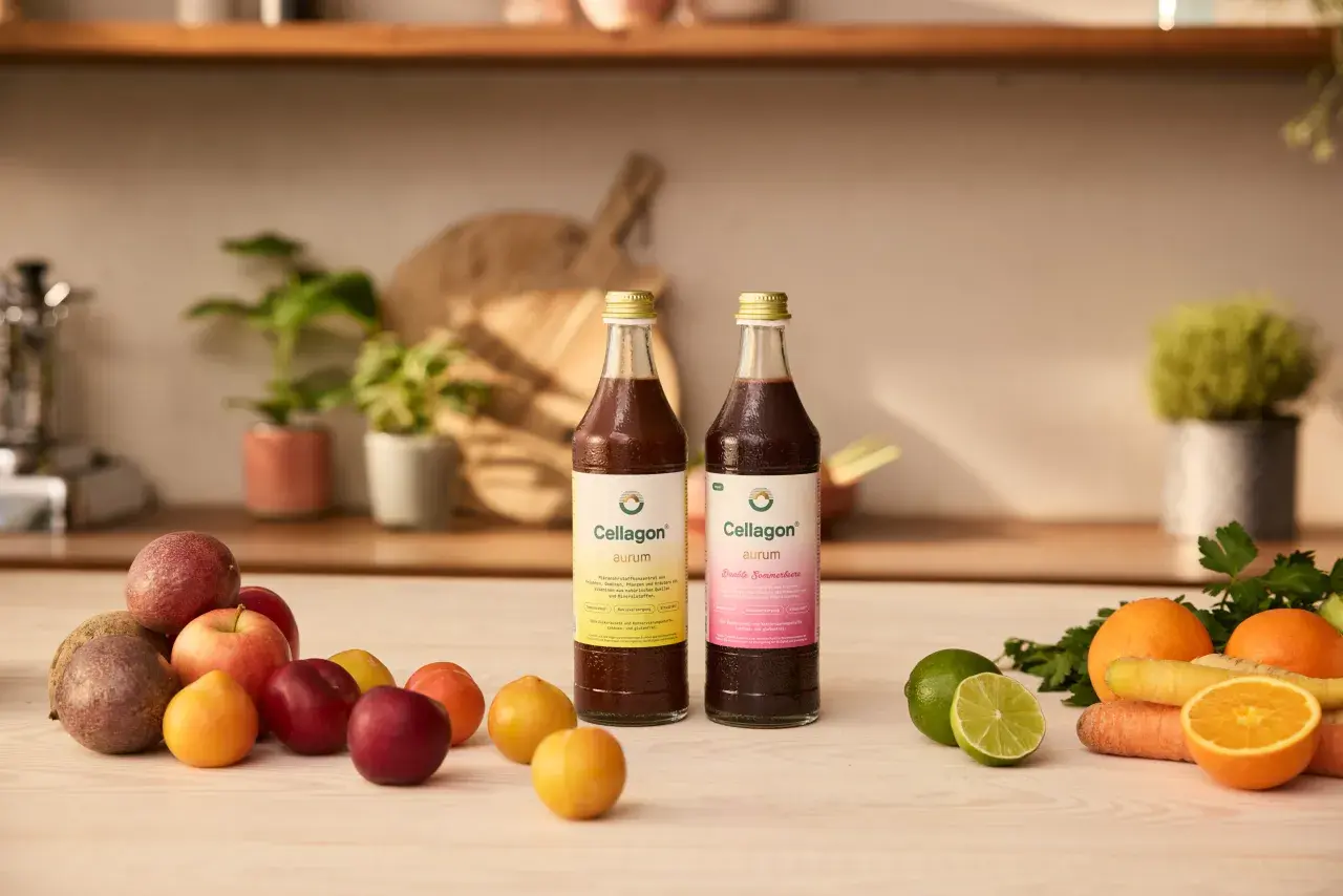 Zwei Flaschen Cellagon Aurum stehen neben frischem Obst und Gemüse. Ideal, um Eisen und Vitamin D zusammen einzunehmen für Vitalität.