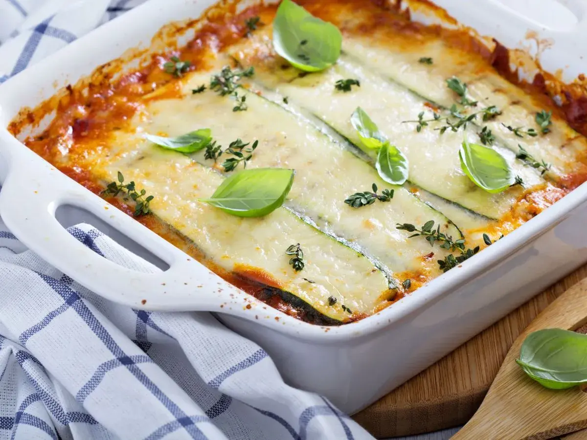 Pyszne lasagne z cukinią, zapieczone pod ciągnącym serem, ozdobione świeżą bazylią i tymiankiem.