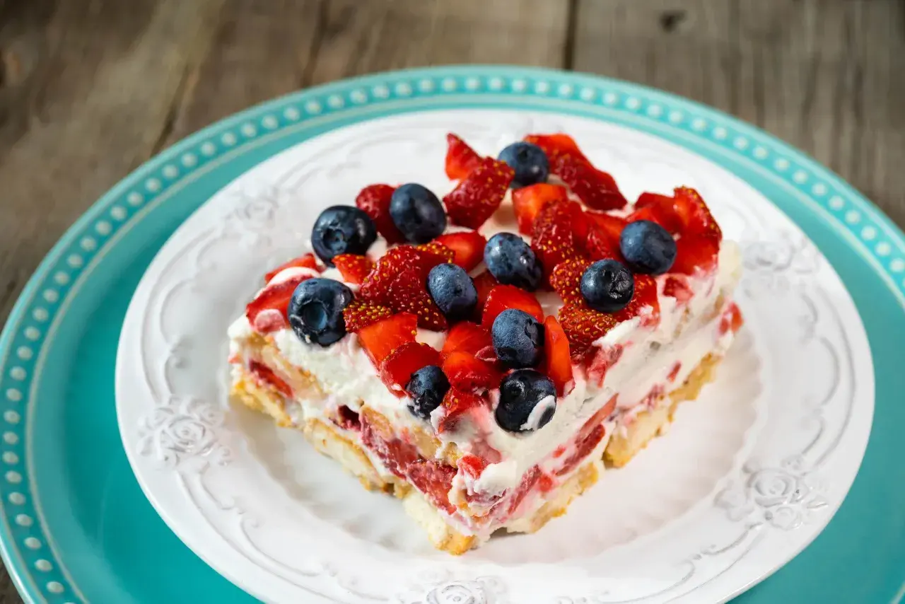 Tranche de tiramisu aux fruits rouges, garnie de fraises et myrtilles fraîches, sur une assiette blanche ornée.