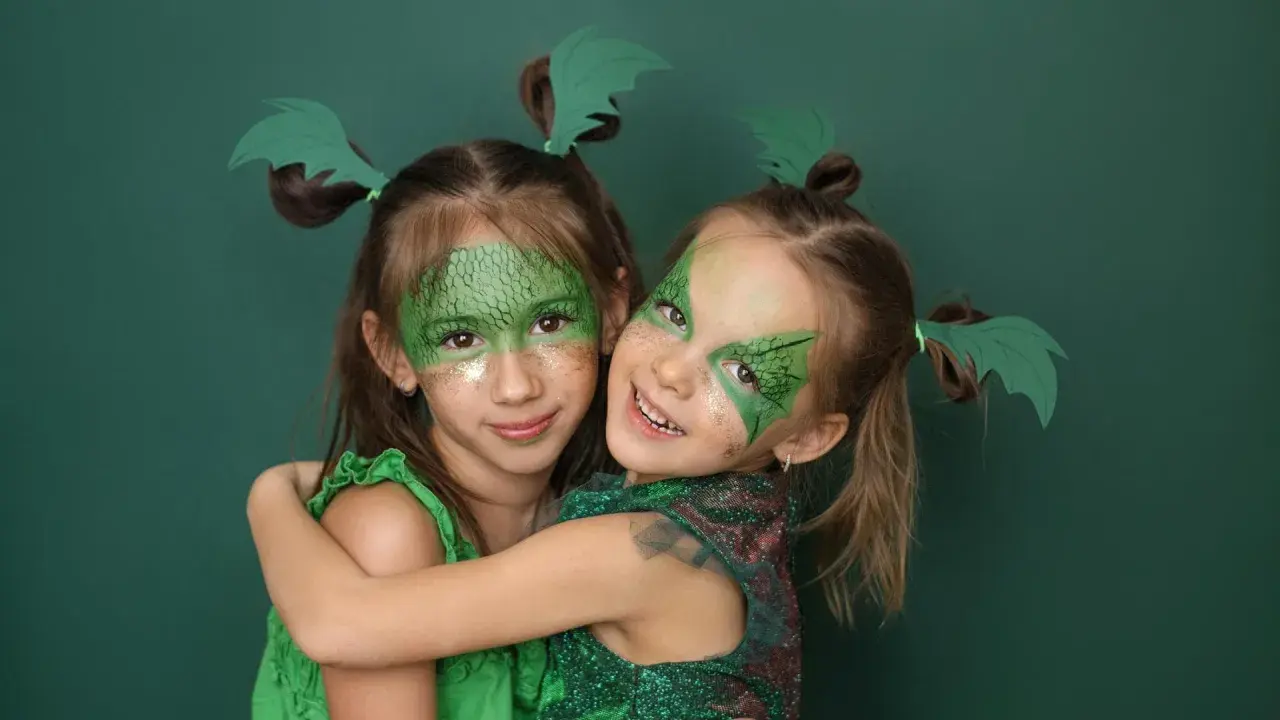 Zwei Mädchen mit Drachenschminke und grünen Flügeln im Haar, ein einfaches Drachen-Kinderschminken-Ergebnis.