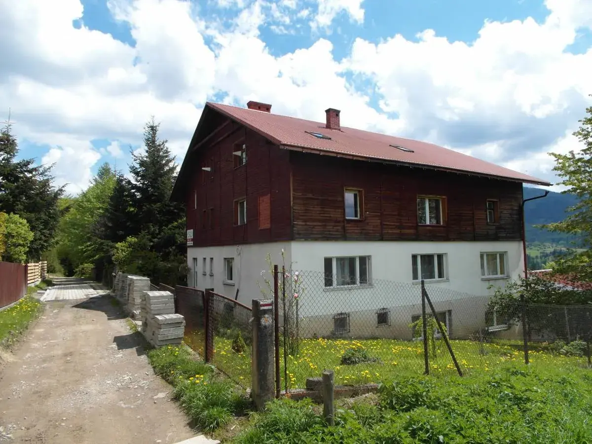 Stacja turystyczna Abrahamów, drewniano-betonowy budynek z czerwoną dachem, otoczony zielenią i polnymi kwiatami.