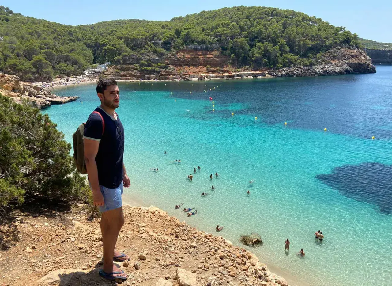 Un hombre con mochila admira una cala turquesa en Ibiza. ¡Un plan perfecto que ver en Ibiza en 4 días!