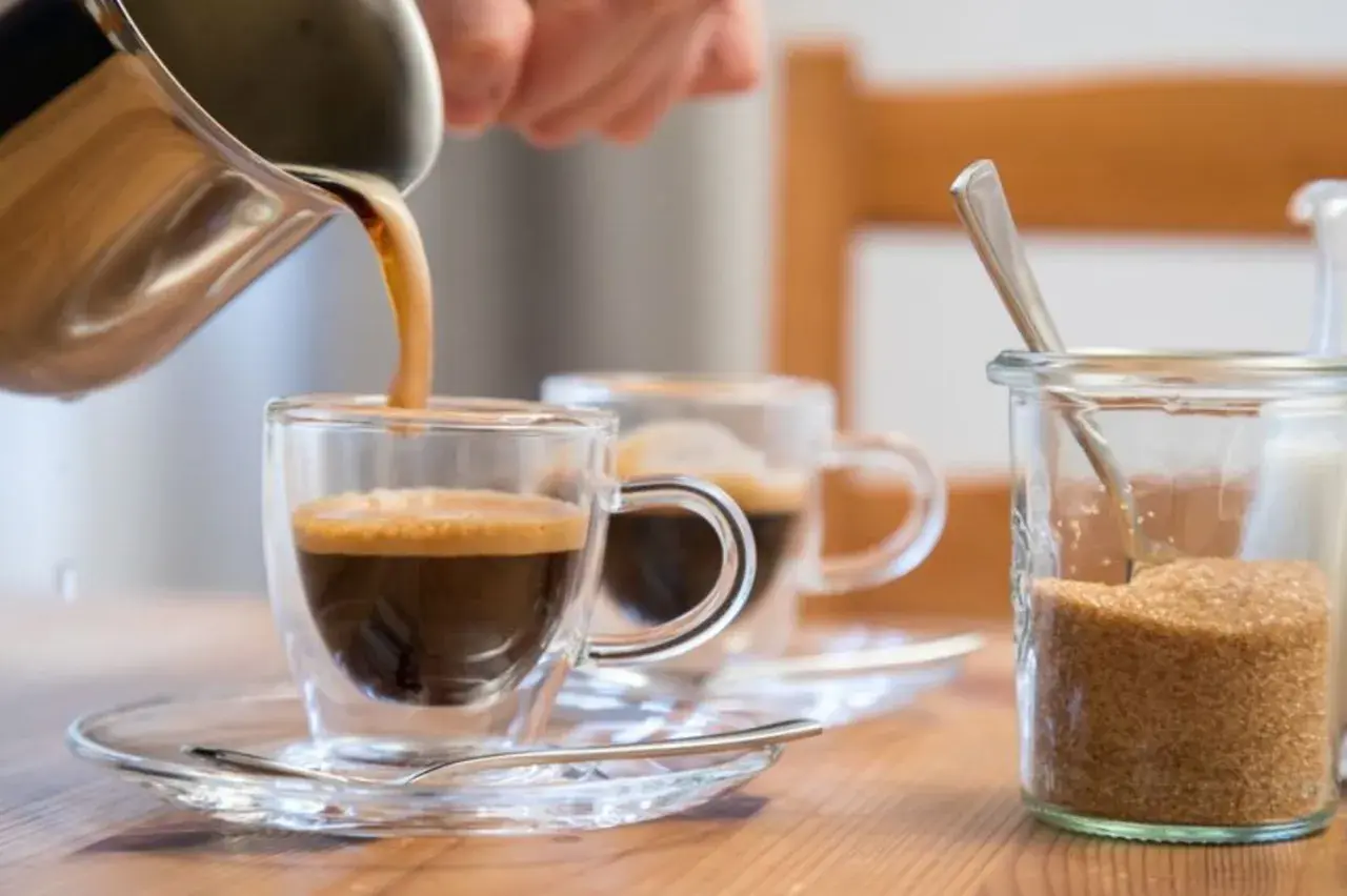 Frisch gebrühter Kaffee wird in ein Glas gegossen. Ob Kaffee den Blutdruck beeinflusst, ist eine häufige Frage. Daneben steht Zucker.