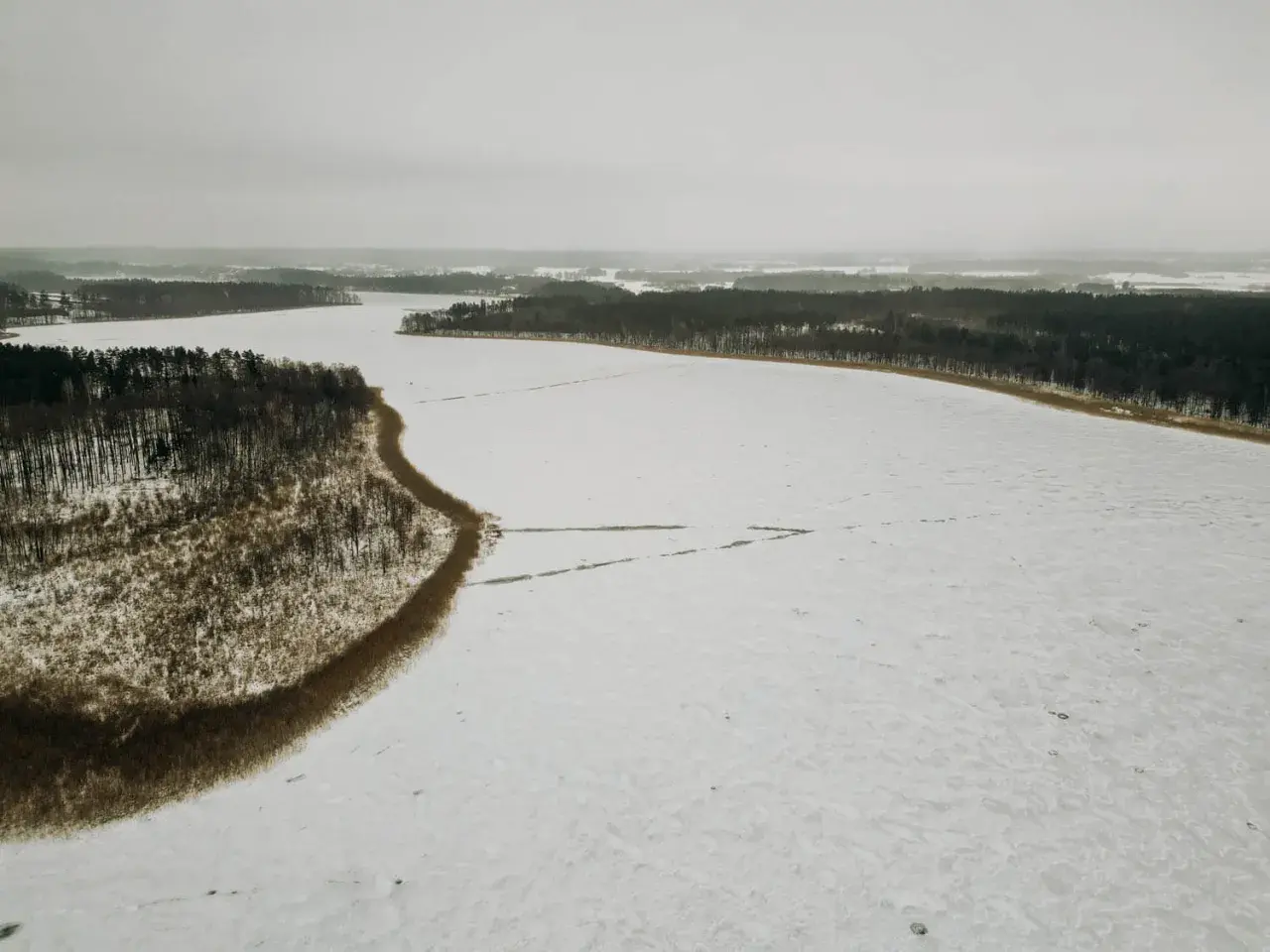 Zimowy krajobraz: zamarznięte jezioro Tyrkło otoczone lasem. Śnieg pokrywa taflę wody, tworząc białą, rozległą przestrzeń.