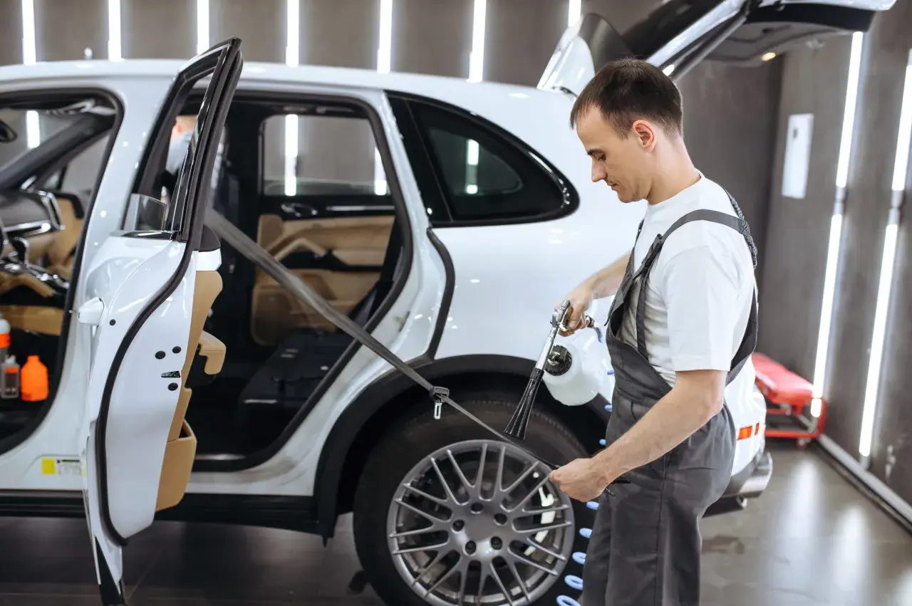 Pracownik detailingu samochodowego pokazuje, jak prać pasy bezpieczeństwa w białym SUV-ie, używając specjalistycznego sprzętu.
