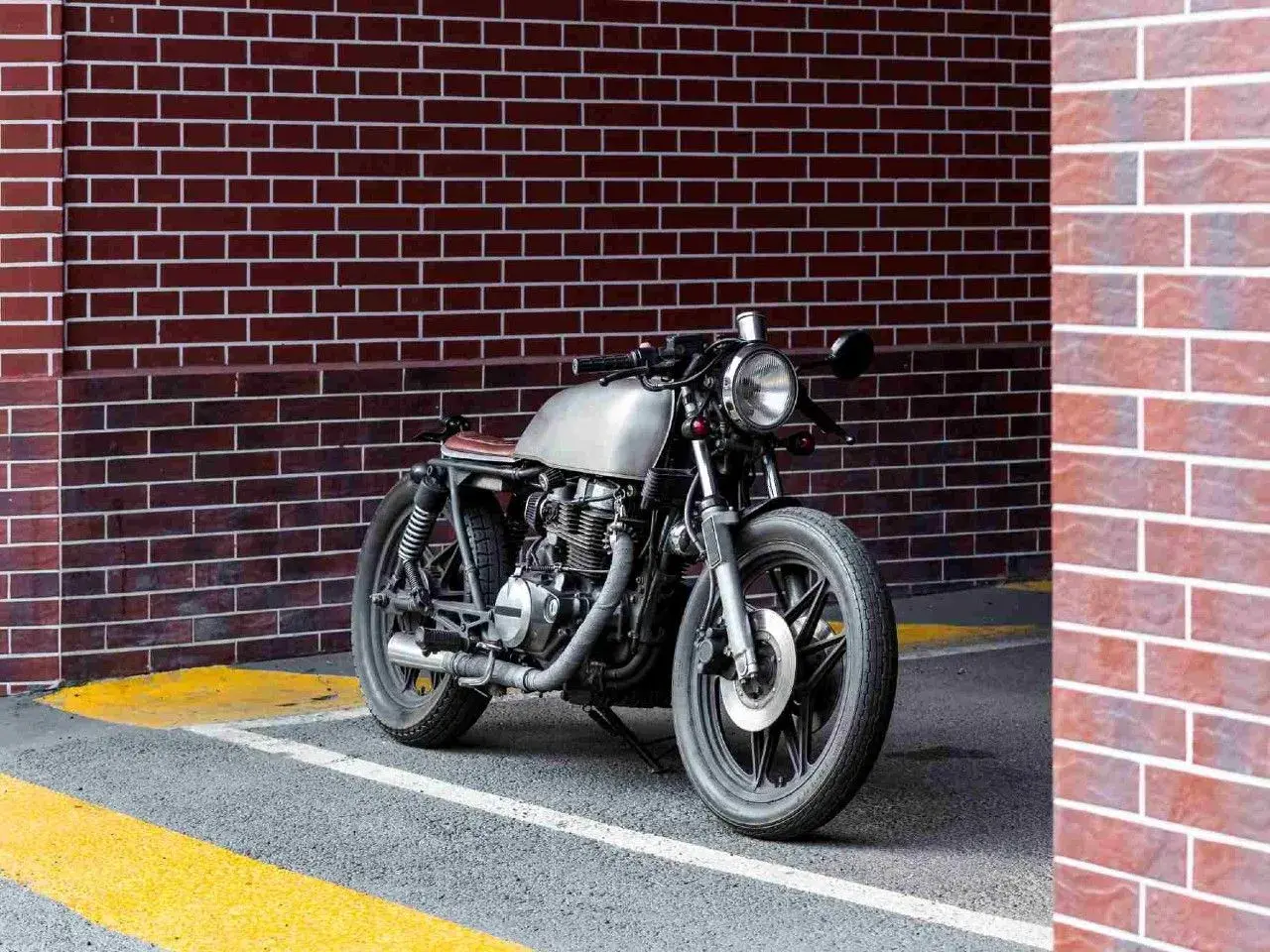 Stylowy motocykl miejski z metalicznym bakiem i brązowym siedzeniem stoi przy ceglanej ścianie.