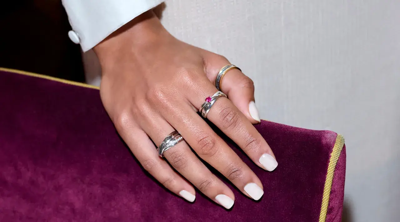Mano con varios anillos, uno de ellos en el dedo anular con una piedra rosa.