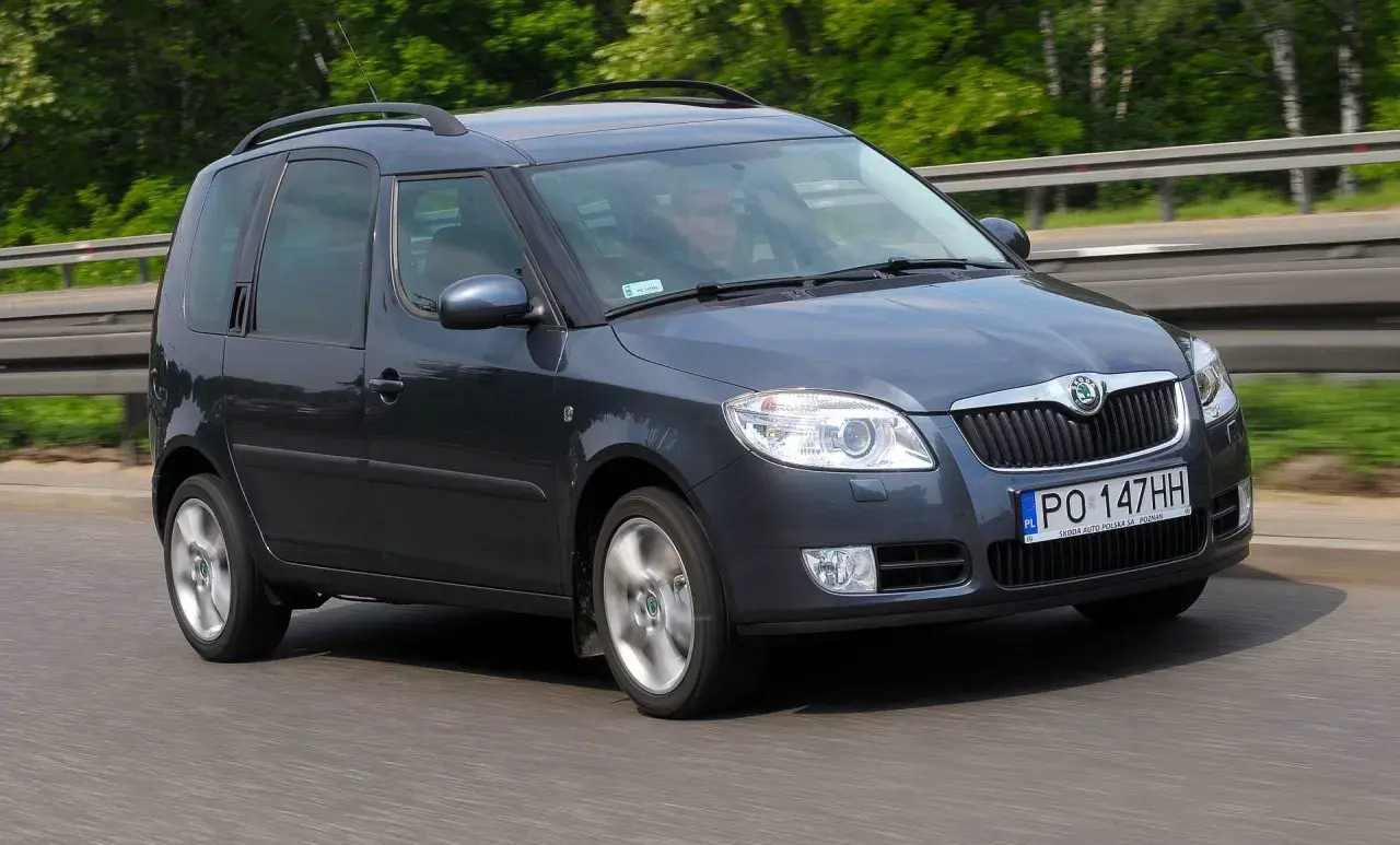 Ciemnoszara Skoda Roomster jedzie po drodze, za kierownicą siedzi mężczyzna.