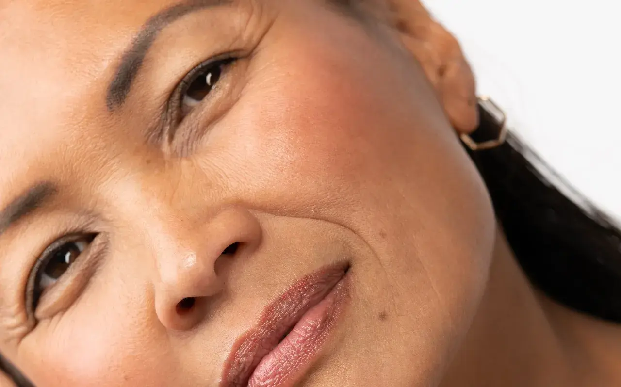 Primer plano de un rostro femenino, mostrando los signos de envejecimiento de la piel, como arrugas finas alrededor de los ojos y la boca.