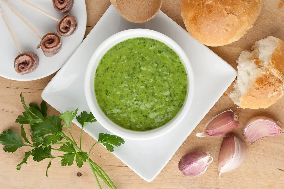 Salsa verde ricetta: prezzemolo fresco, aglio, acciughe arrotolate e pane croccante, ingredienti per un sapore intenso.