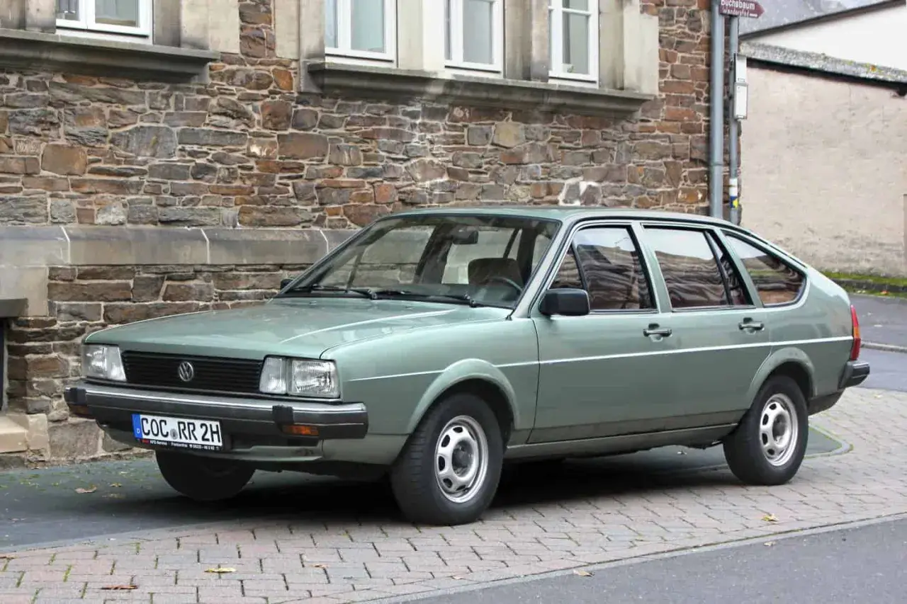 Zielonawy Volkswagen Passat, klasyk z lat 80., parkuje przed kamiennym budynkiem.
