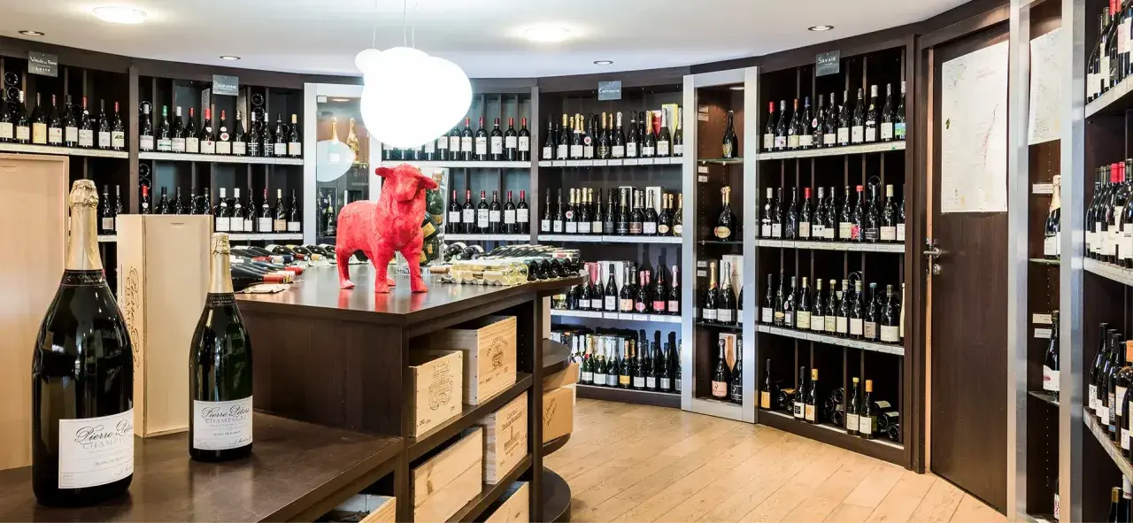 Cave à vin avec étagères remplies de bouteilles, une statue de taureau rouge et des bouteilles de champagne au premier plan.