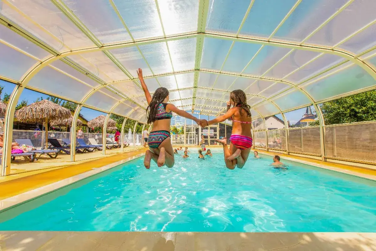 Deux filles sautent main dans la main dans une piscine couverte. Vacances en camping-car à Saint-Malo.