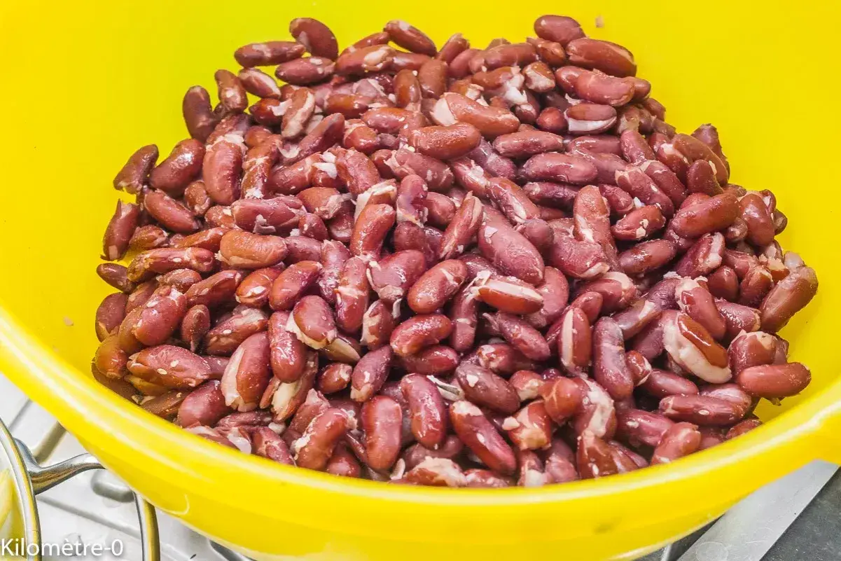 Gros plan sur des haricots rouges dans un bol jaune, prêts pour la cuisson. Ils sont brillants et humides, promettant un plat savoureux.